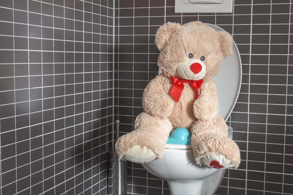 A teddy bear sits atop a clogged toilet