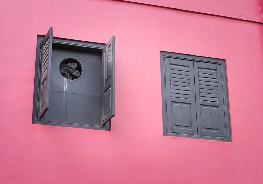 A window fan for cooling sits inside a pink-painted house