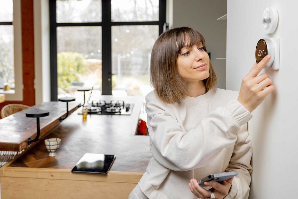 woman adjusting the temperature in her home with a smart thermostat