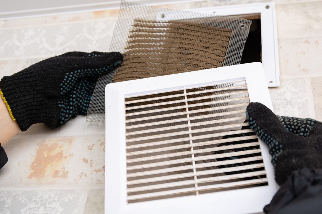An HVAC technician is cleaning a dirty air duct filter