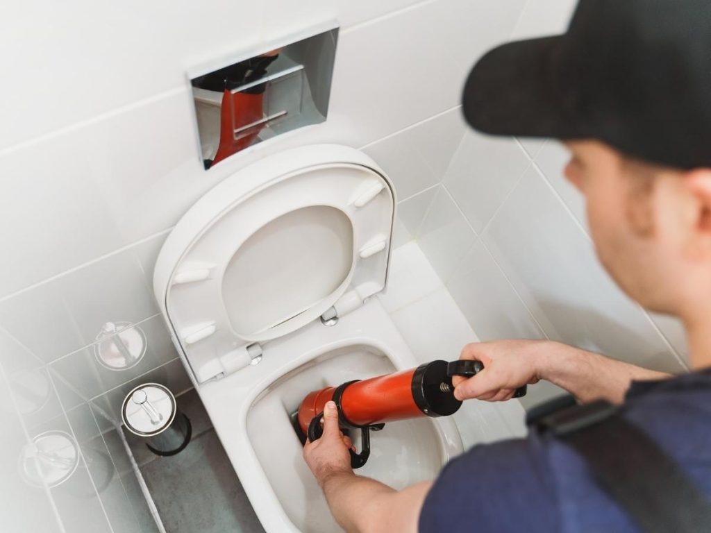How to unclug a toilet without a plunger: a plumber uses an auger tool to remove a clog.