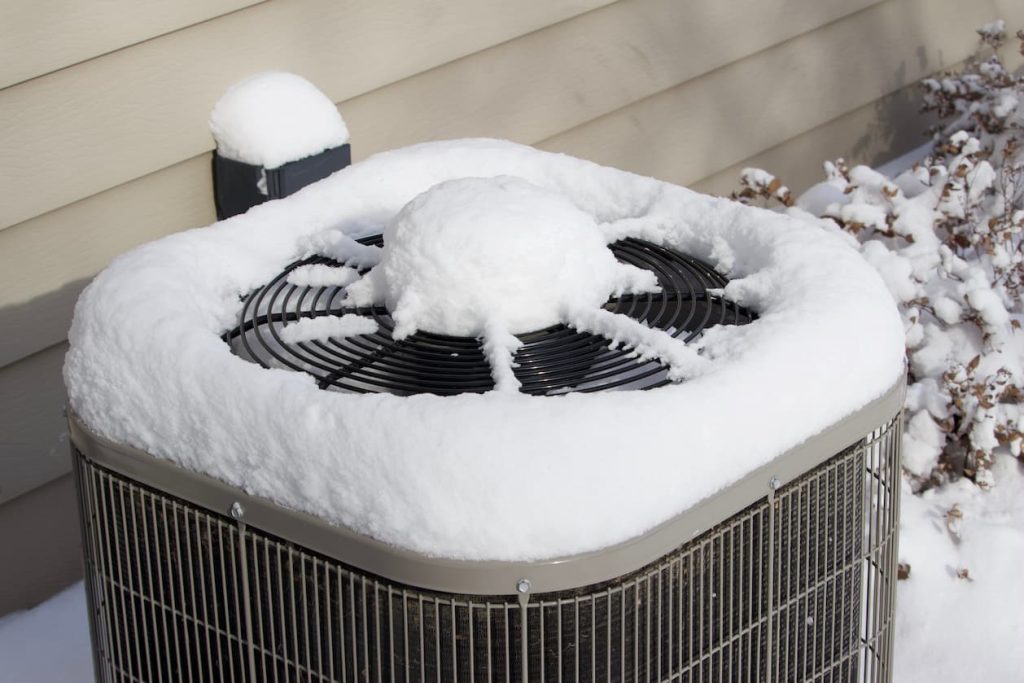 An AC unit covered in snow. It's vital to prepare your air conditioner for winter to make sure it's good by spring.
